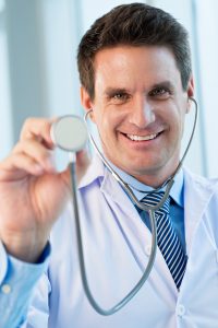 smiling male doctor in a lab coat holding a stethoscope up to the camera