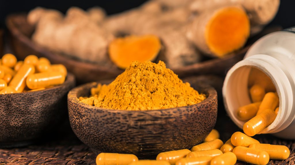 several-bowls-of-turmeric. One-bowl-of-fresh-turmeric-root-a-bowl-of-ground-up-turmeric-powder-and-a-bowl-of-turmeric-in-capisule-form. Bottle-of-turmeric-capsules-spilled-in-front-of-the-bowls