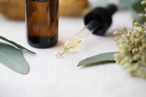 A vial contailing eucalyptus oil on a table with an eye dropper and several eucalyptus leaves next to it