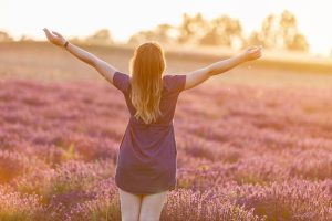 A young woman arms stretched out in the fading sun in a lavendar field