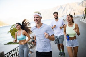 four young adults wearing workout clothes  smiling and jogging on a bike path 