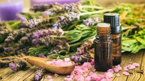 lavander stalks laying on a wooden table with vials next to it containg lavander oil. 