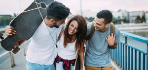 one young man holding a skateboard walking arm in arm with another young man and woman. They are smling and laughing