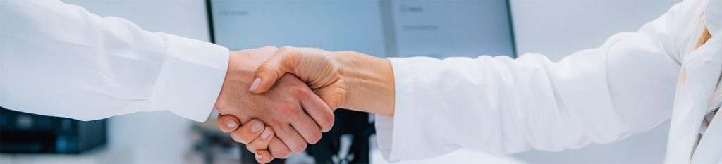 doctor in white lab coat and a male in a long white button down shirt shaking hands in agreement