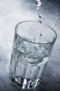 half full cup of water with large drops of water falling into the cup