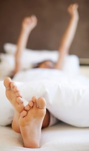 young woman stretching her arms up in a bed with a white comforter and pillowcases